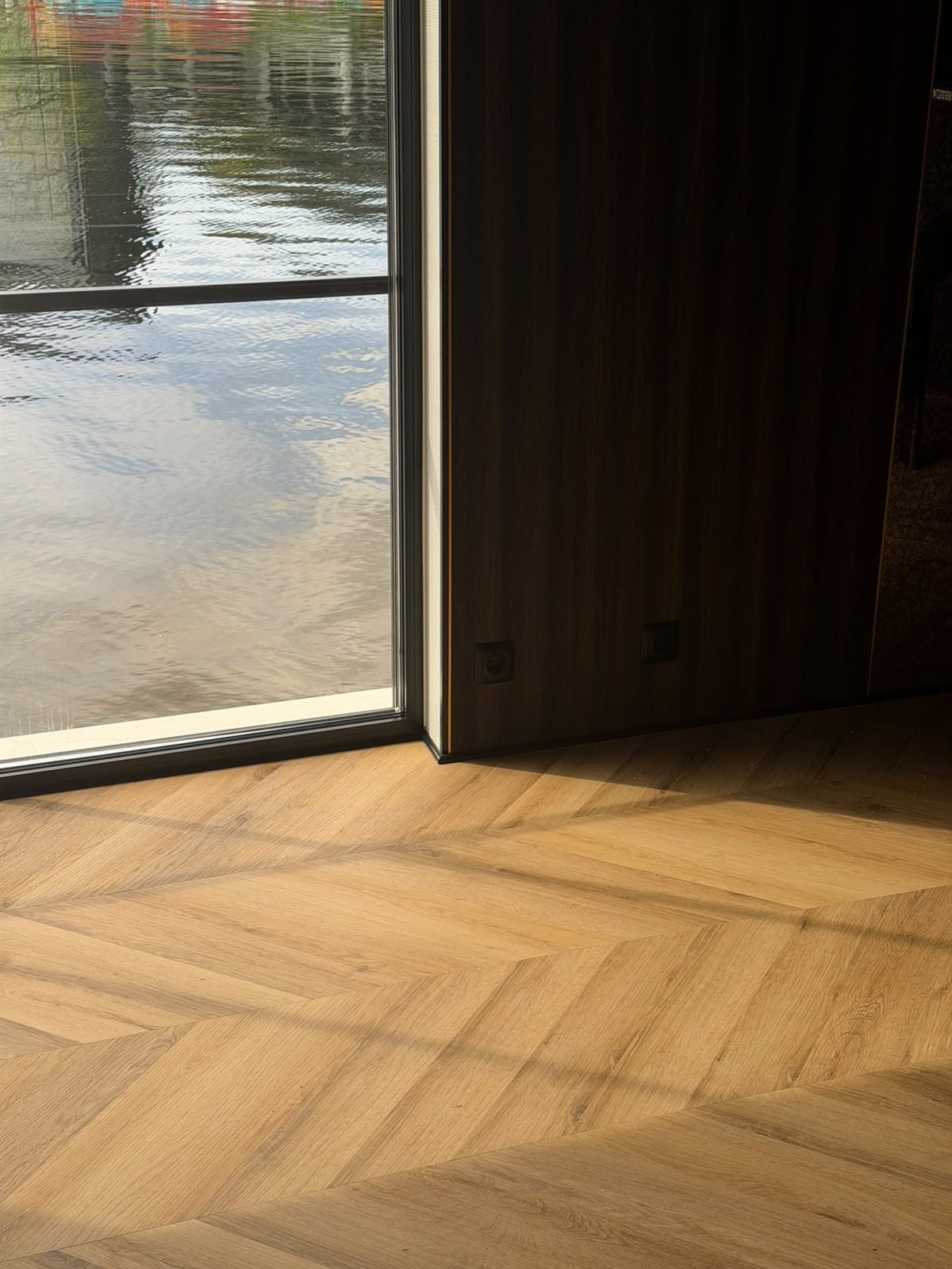 Oak chevron floor, dark timber wall and a full-height window onto the water
